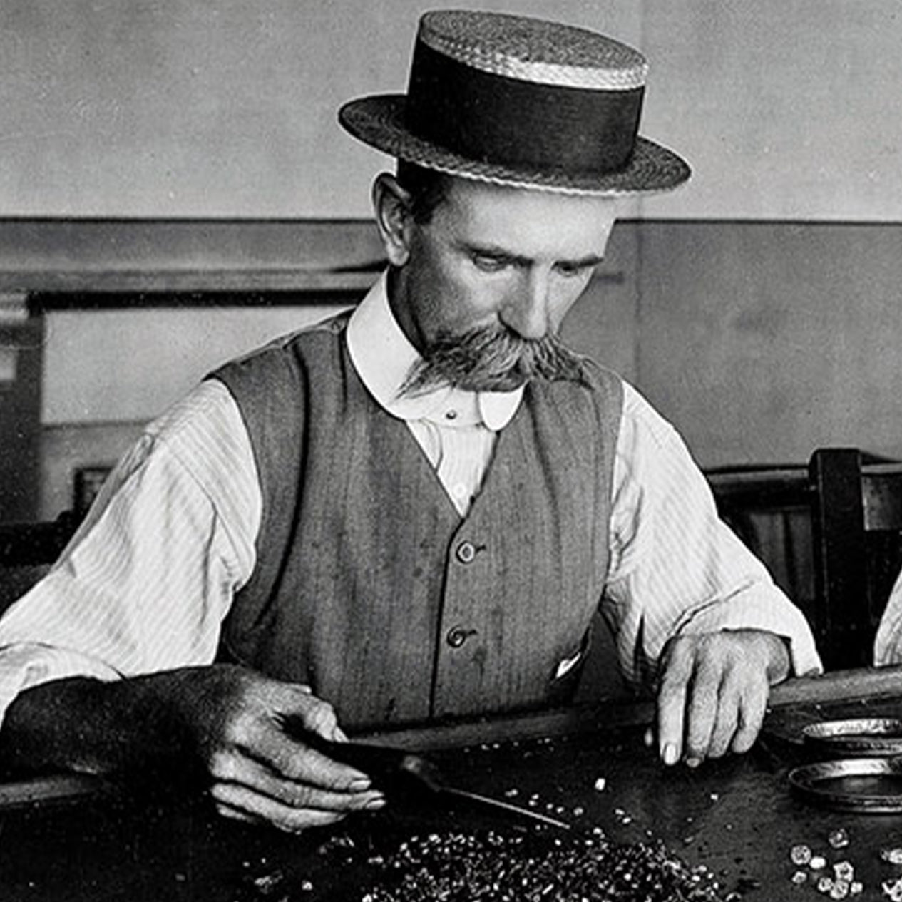 Historical image of a man inspecting and sorting rough diamonds at the Kimberly Mine